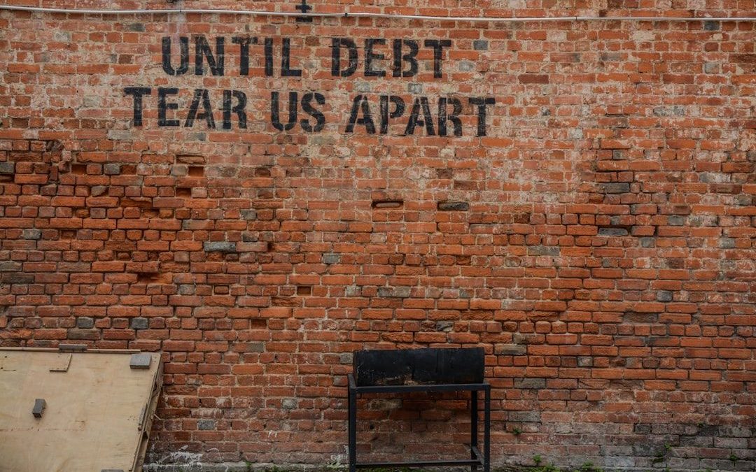 A close‑up photograph of brick wall displaying the words "until debt tear us apart"; the image conveys the seriousness and administrative tone associated with managing tax debt obligations in New Zealand.
